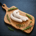 Saucisses blanches nature sur planche en bois d'olivier, fond ardoise